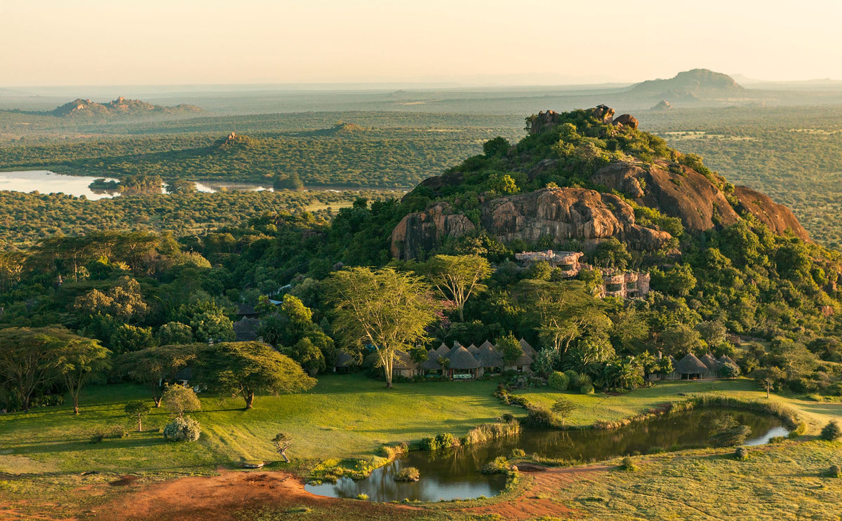 Safari camp at the base of a rocky outcrop in a vast African savannah with a lake and river