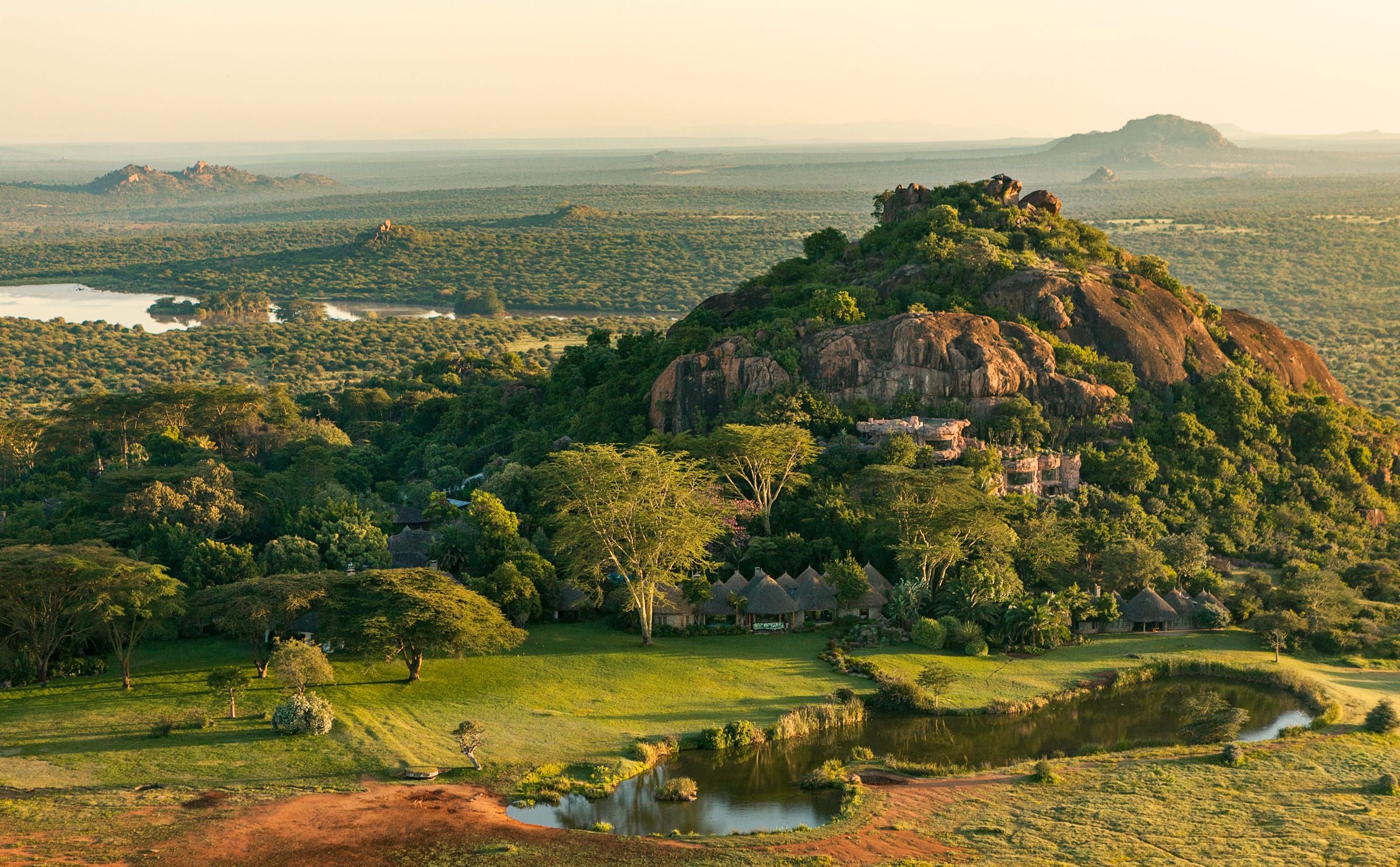Safari camp at the base of a rocky outcrop in a vast African savannah with a lake and river