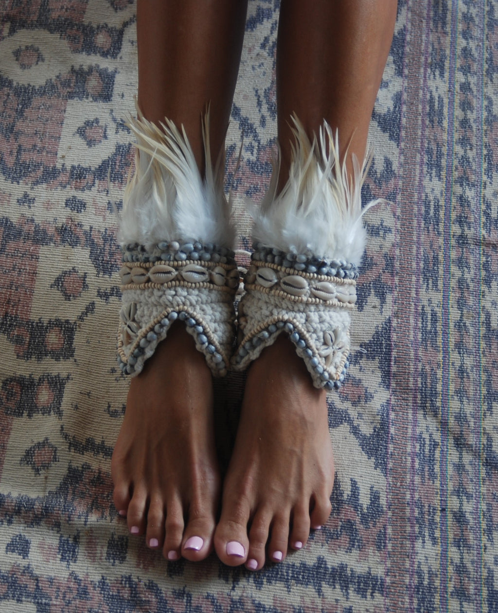 Feet wearing ornate cream ankle cuffs with feathers on a patterned fabric background