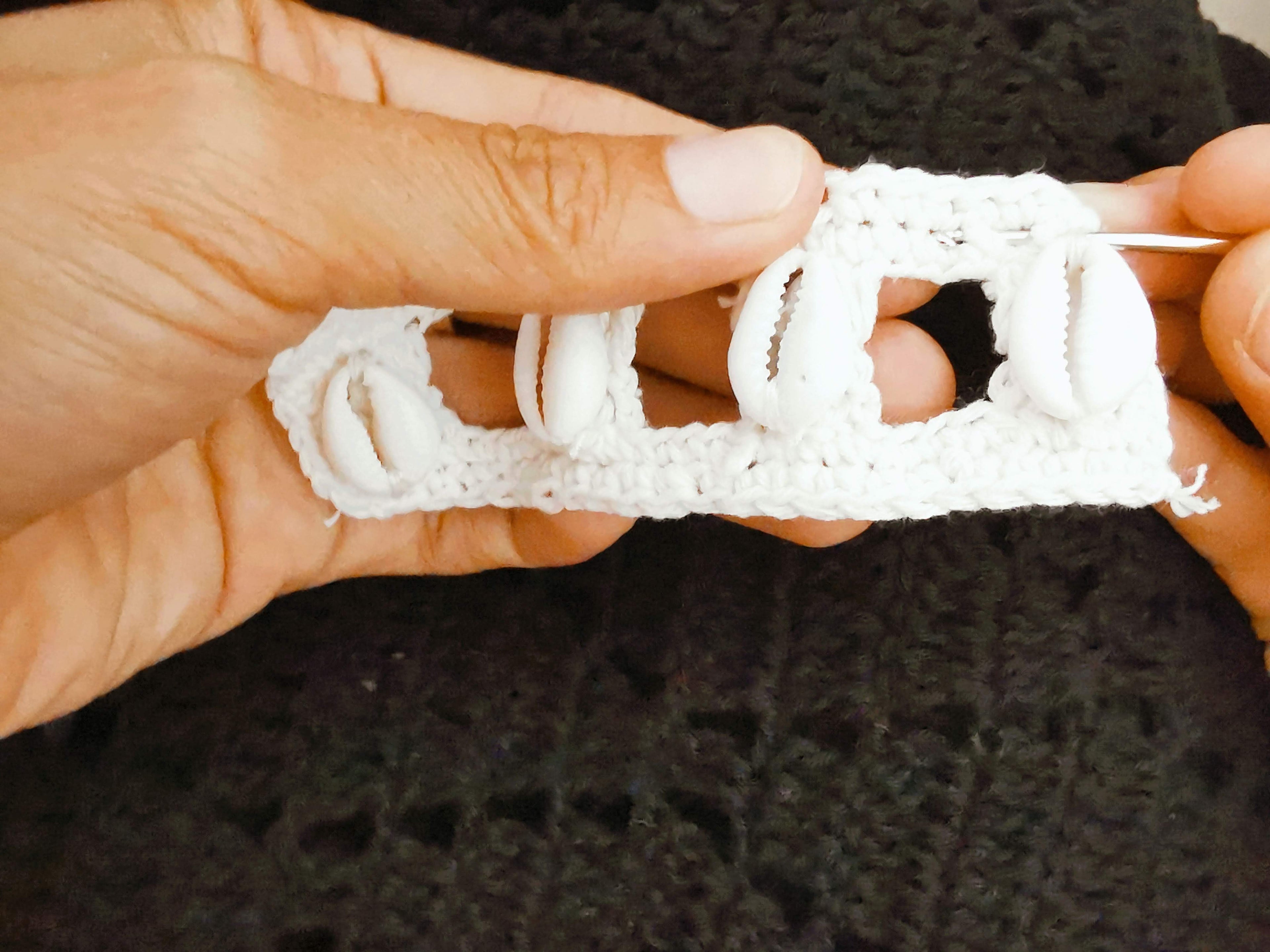 Shells being sewn on white crocheted item held in a hand against a dark background