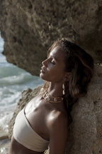 Woman leaning against a rock in cream bikini by the ocean