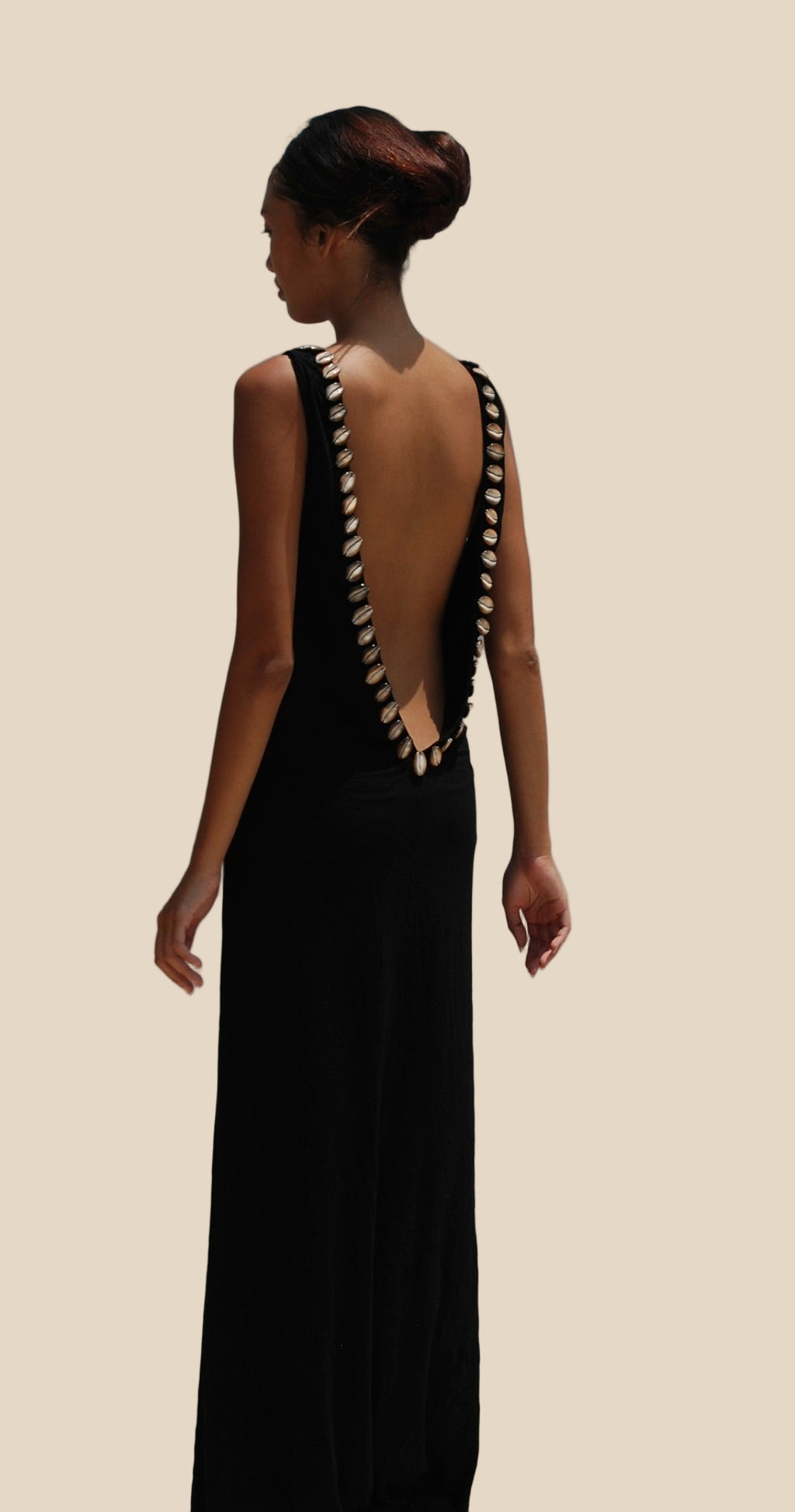 Woman wearing a black long dress with a unique back on a plain background