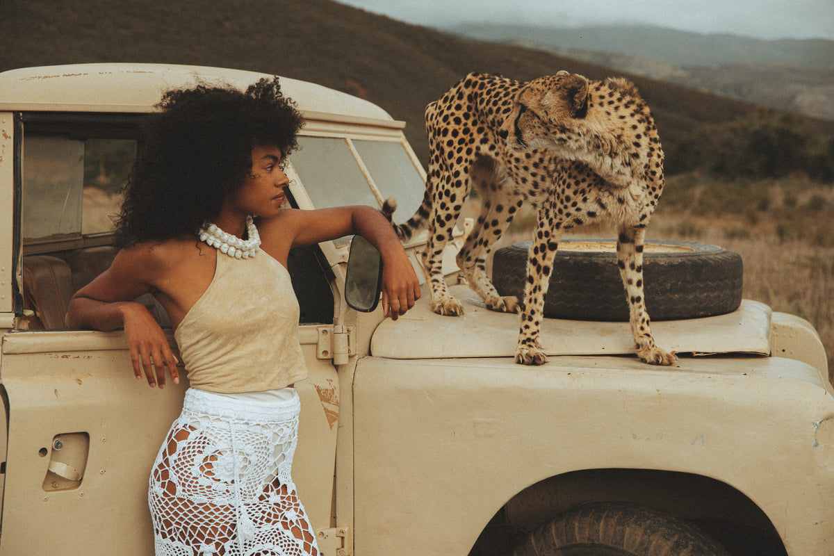 Woman standing next to cheetah on the hood of an off-road vehicle in a natural setting.