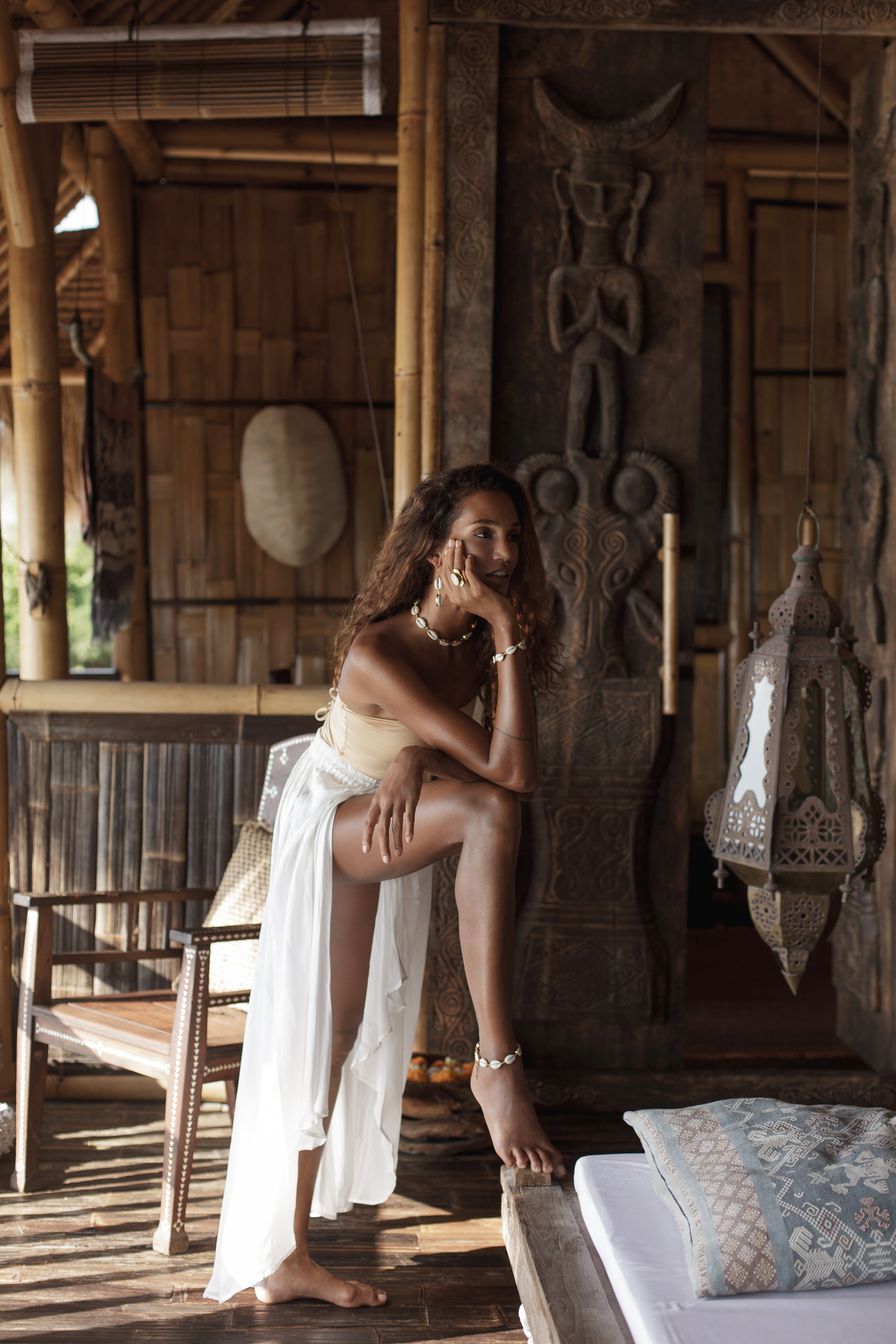Woman in a gold swimsuit and white pants sitting on a wooden bench in a rustic setting in Bali. 