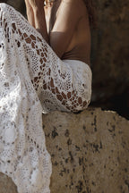 Close-up of a person wearing a lace crochet garment against a textured wall.