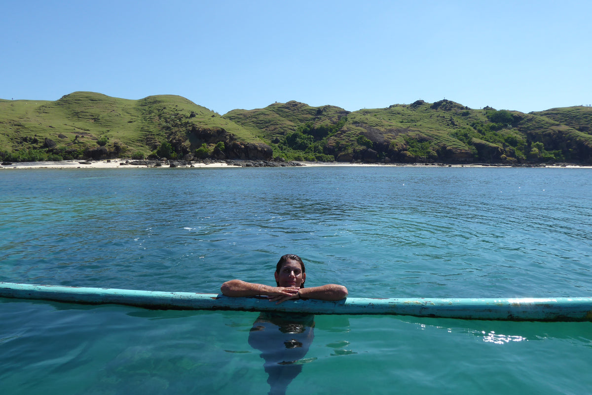 Person holding a blue surfboard in clear blue water with green hills in the background