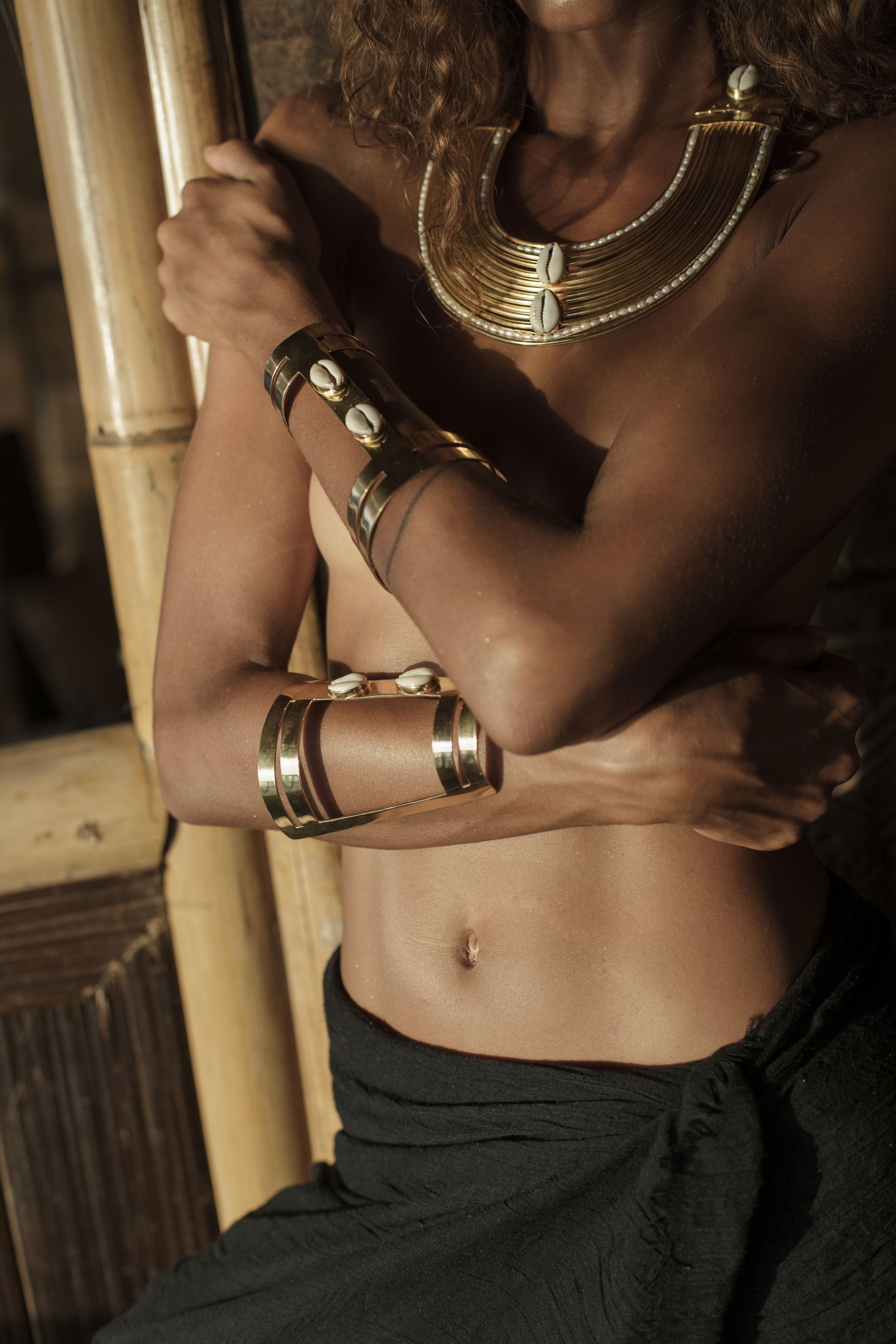 Person wearing gold and shell jewelry and black clothing with a blurred background