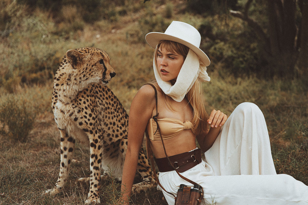 Woman in a safari outfit sitting next to a cheetah in a natural setting