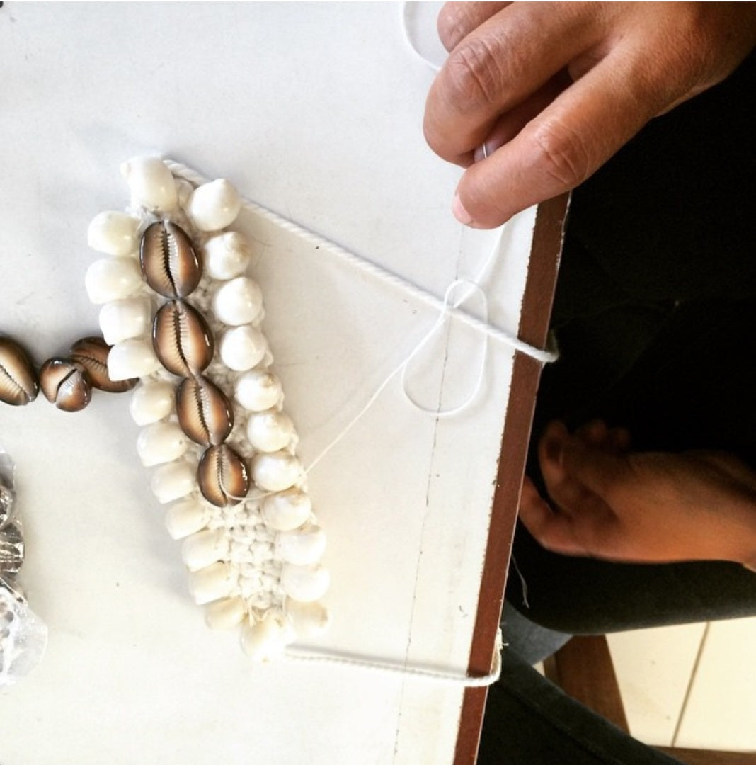 Close-up of a hand holding a white cuff with shell decorations on a light background