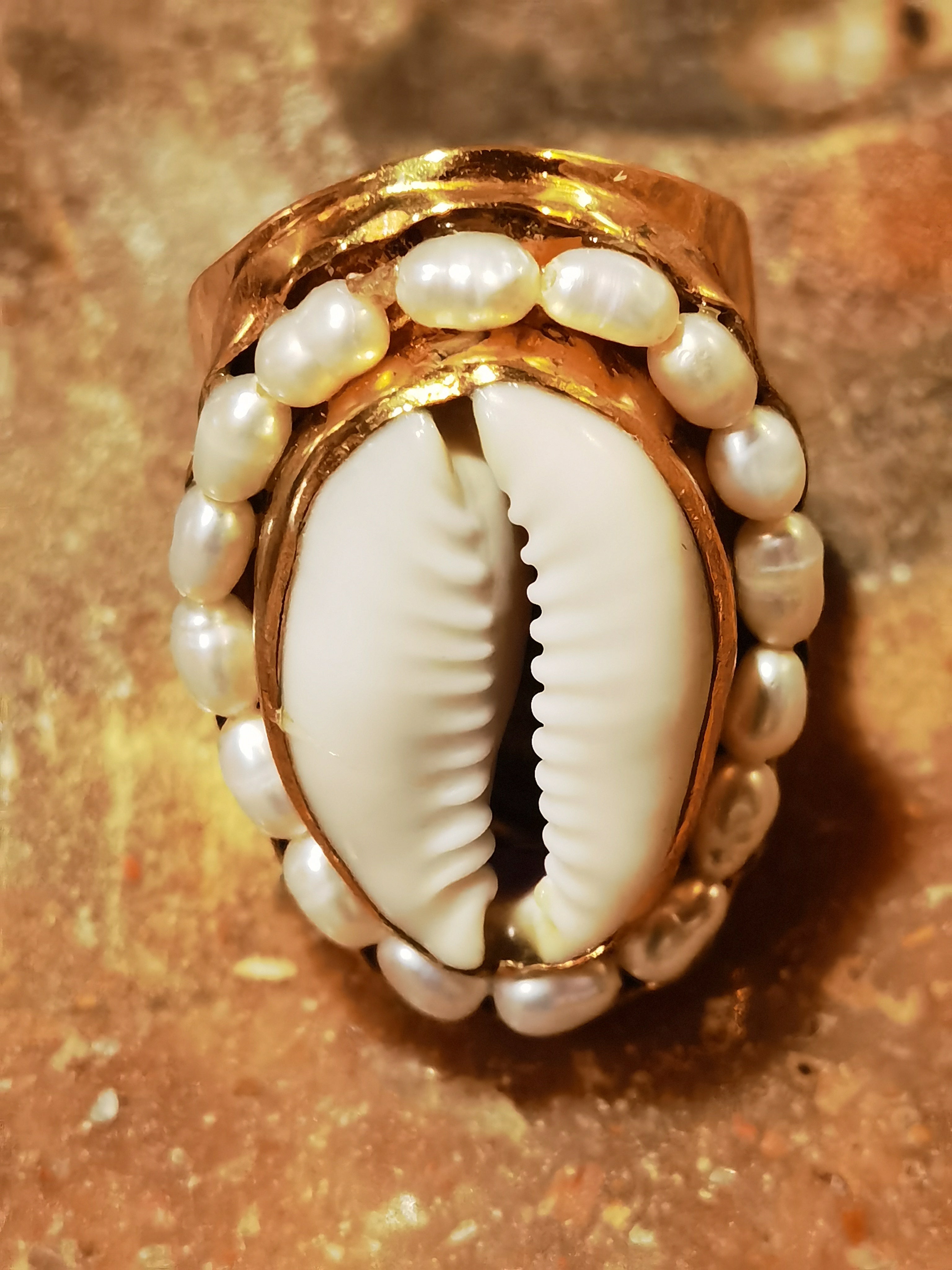 Gold ring with a central shell and pearl-like stones on a textured surface