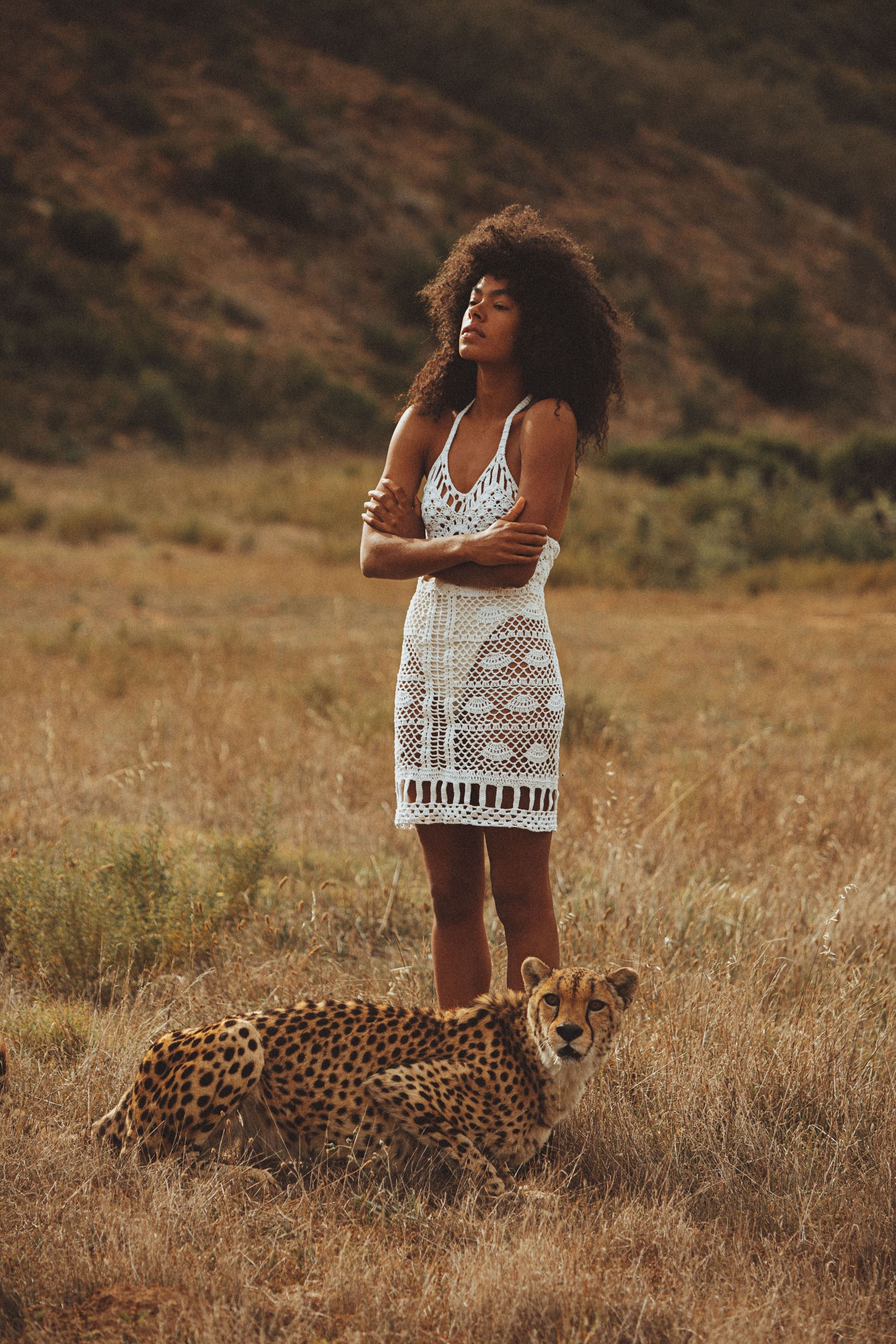 Woman in cream crochet dress in a wild environment with a cheetah