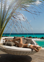 Woman relaxing in a hammock by the ocean with palm leaves in the foreground.