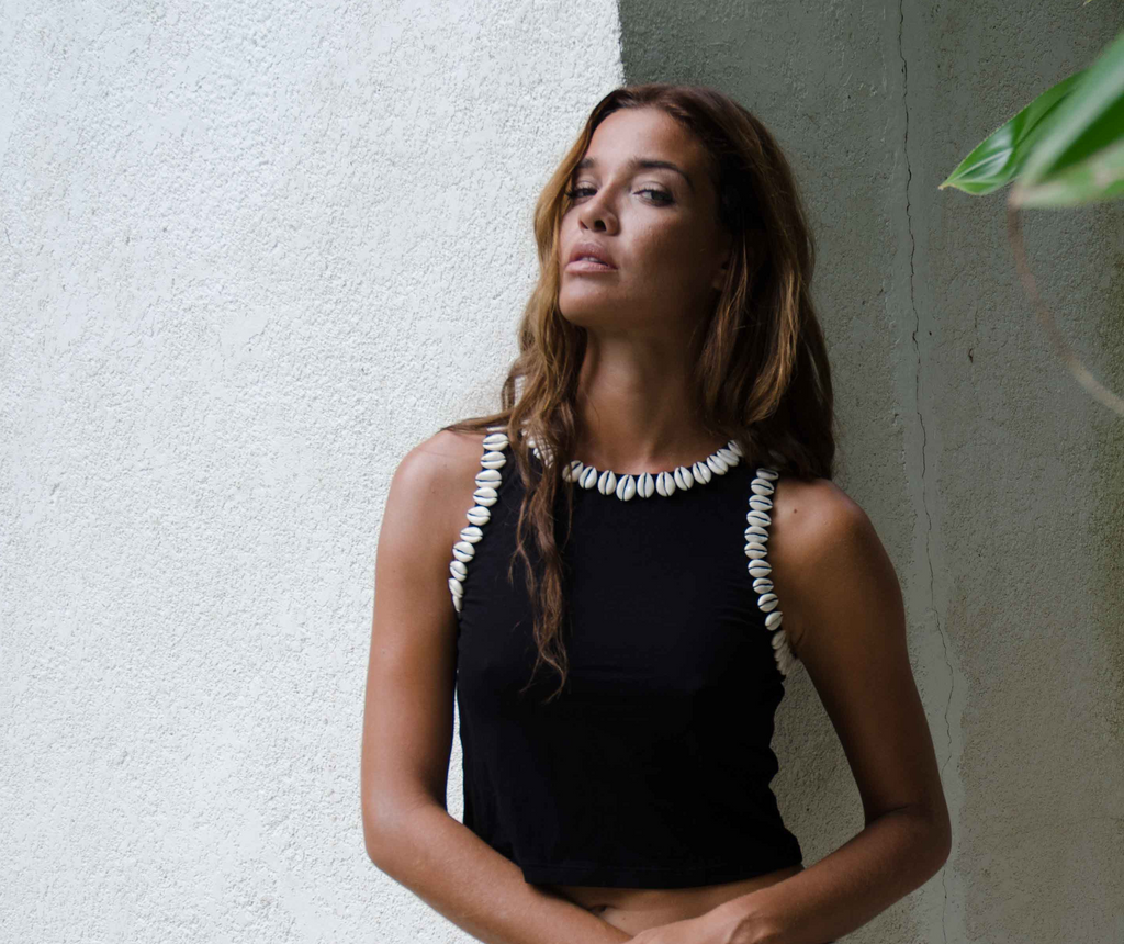 Woman wearing a black top with white shell details against a textured wall.