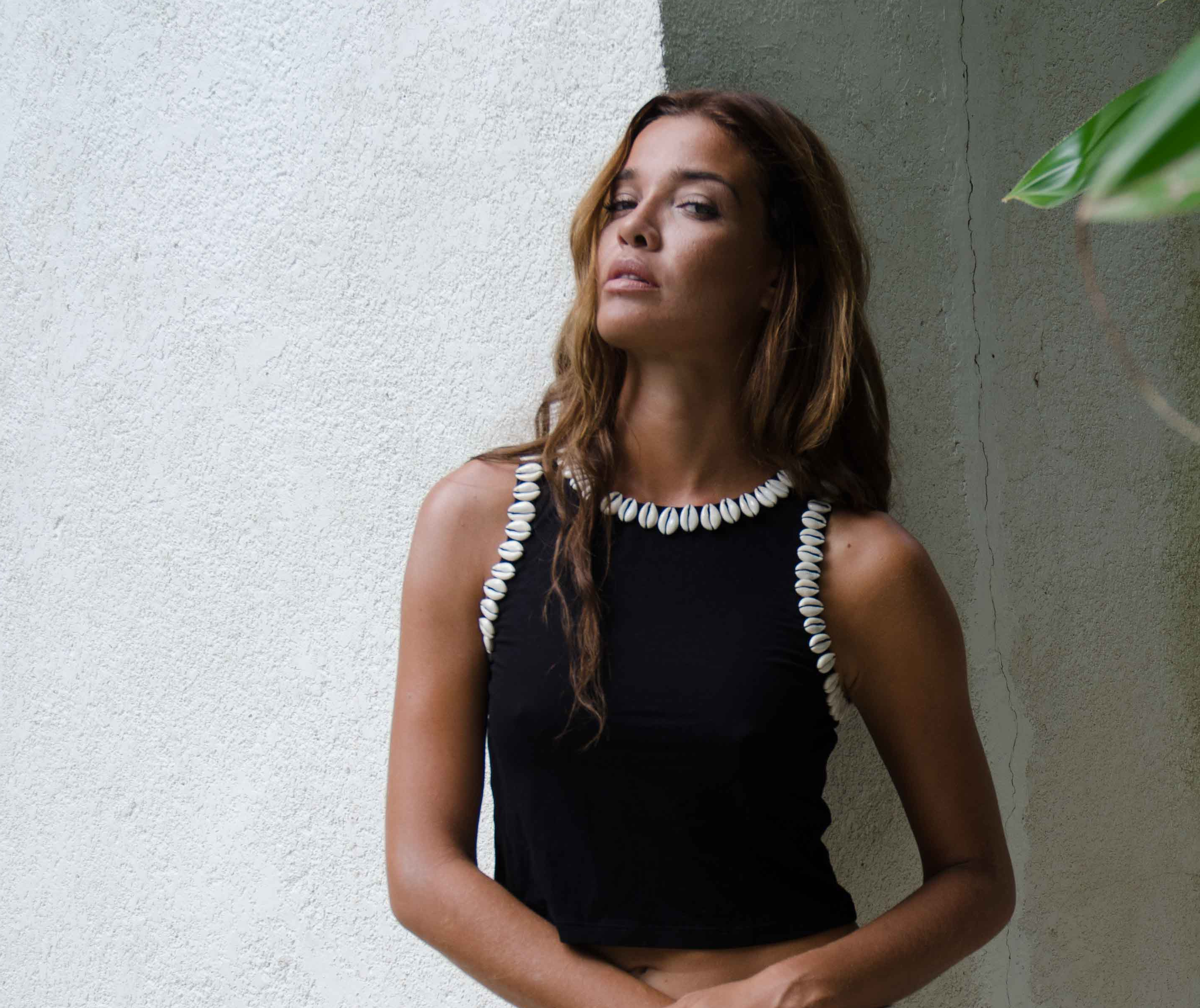 Woman wearing a black top with white shell details against a textured wall.