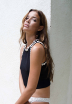 Woman wearing a black sleeveless top and white lace underwear against a light background