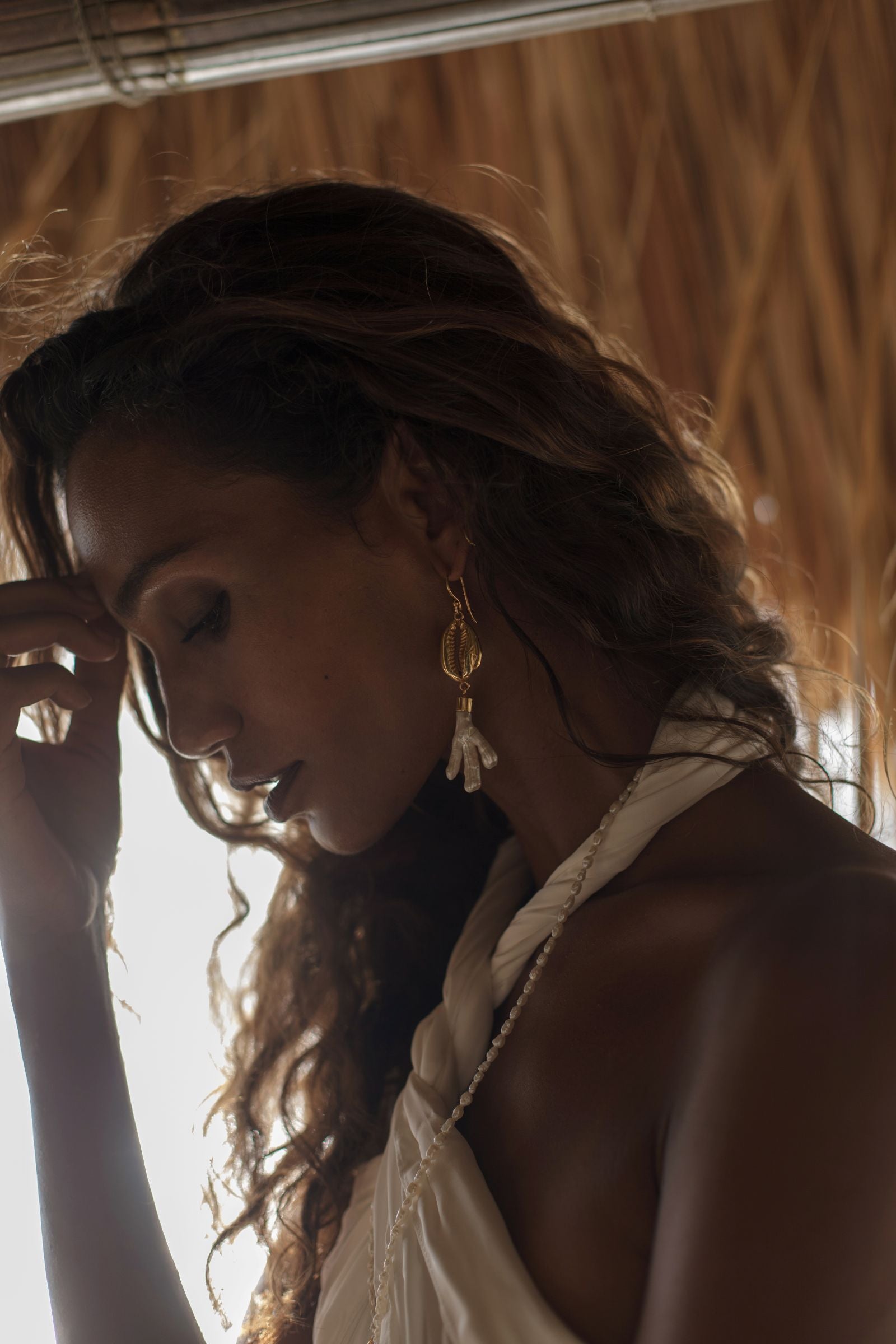 Woman with long hair with god and shell earrings against a natural background
