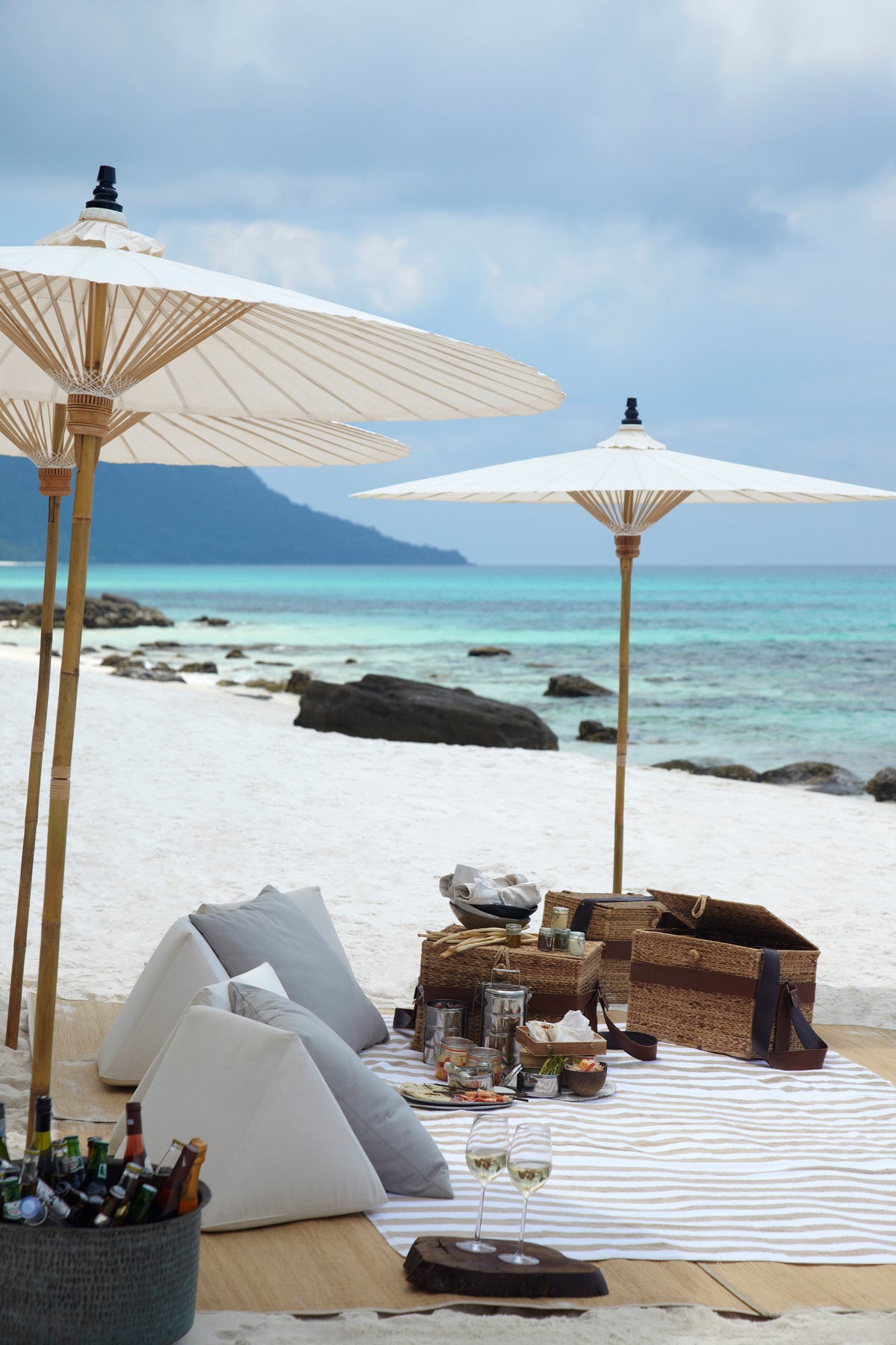 Beachside setting with white umbrellas, chairs, and a table with drinks and snacks.