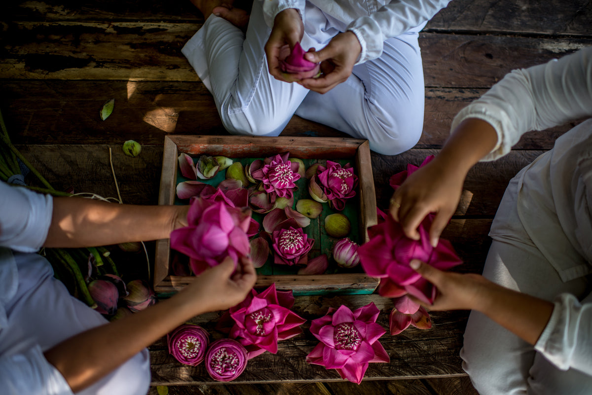 Three people arranging pink lotus flowers on a wooden surface.