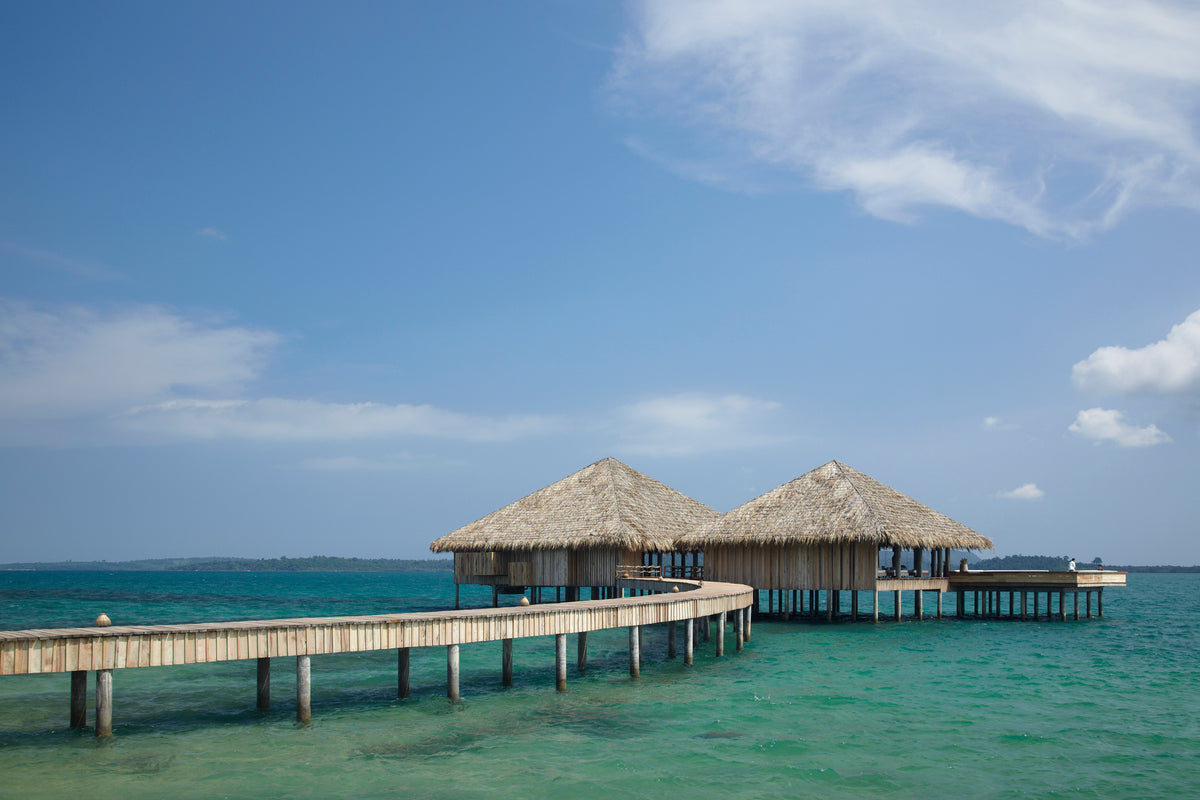 Wooden pier with thatched roof structures extending into the ocean under a clear blue sky.
