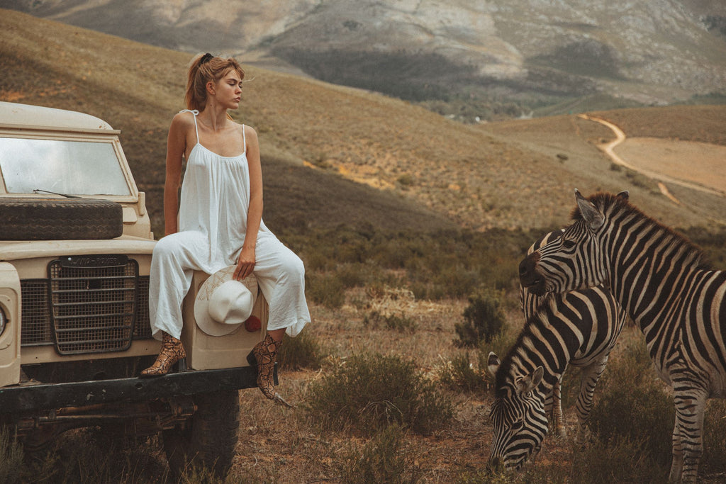 Women in white jumsuit in the savannah on a Land Rover with Zebras