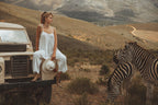 Women in white jumsuit in the savannah on a Land Rover with Zebras