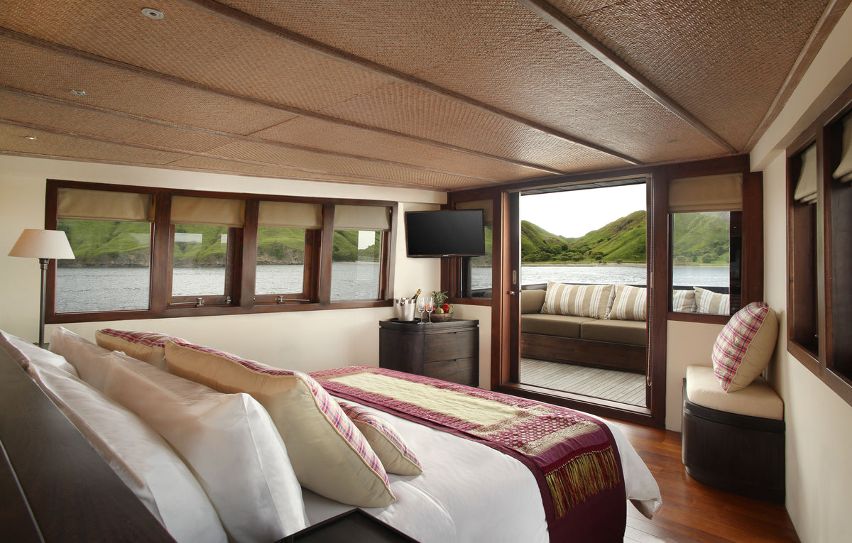 Luxury cabin with large windows, bed, and views of water and hills of Indonesian islands