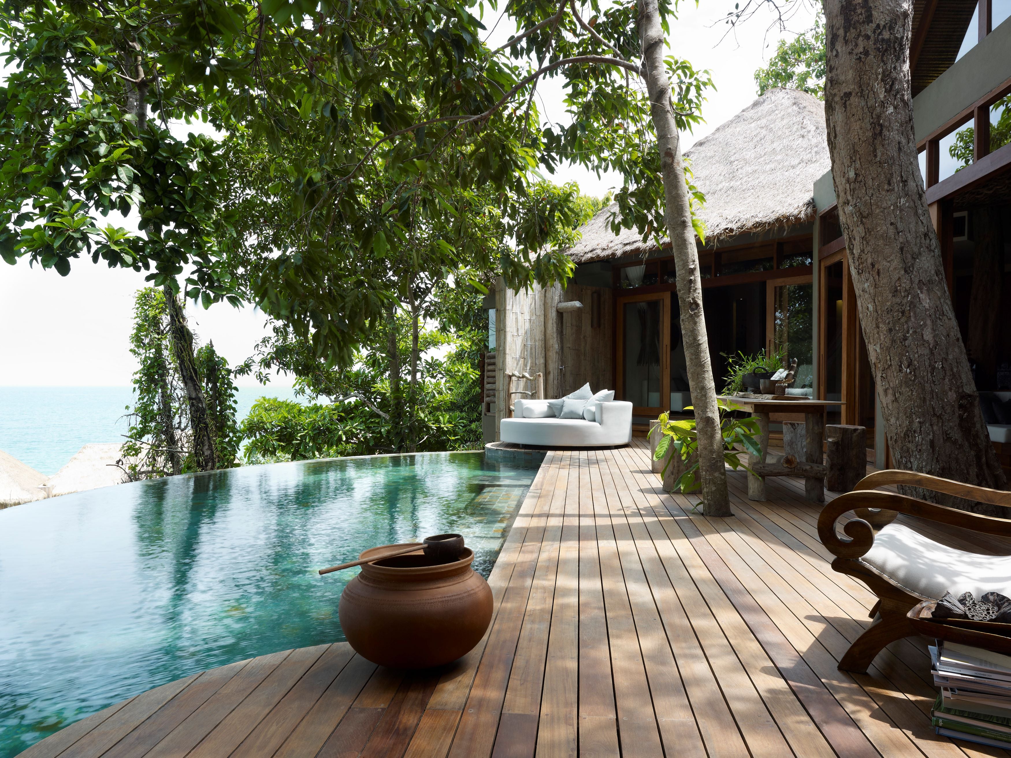 Outdoor pool area with wooden deck, seating, and thatched-roof building.
